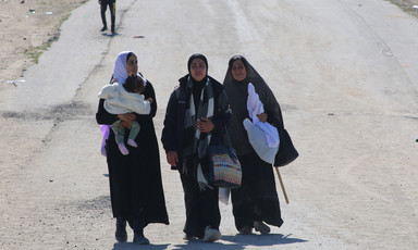 Forcibly displaced women carrying their belongings walk past Israeli forces
