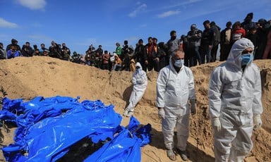 A number of men wearing white overalls and masks stand beside corpses in body bags on a beach in southern Gaza 