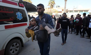 A man carries an injured child beside an ambulance in Gaza 