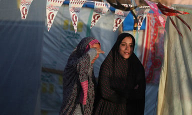 Two women stand under bunting hung up between tents in Gaza 
