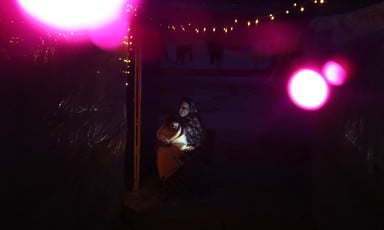 Two large pink lights glow in the dark, with a woman and child in the backgroud