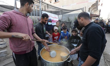 Three men serve food from a large pot to children in Gaza