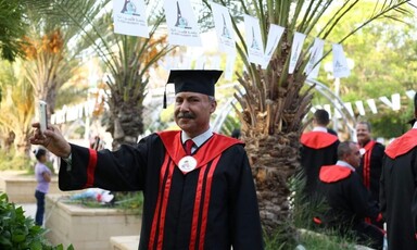 Dr. Abdel Nasser al-Saqqa in full graduation regalia, posing by palm trees. 