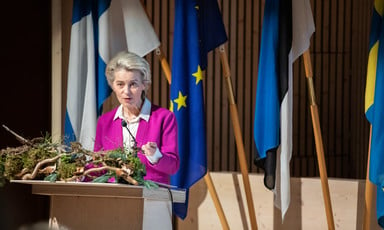 European Commission President Ursula von der Leyen stands in front of a few flags