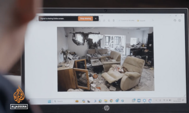 A man with a laptop views an image of a war-ravaged home