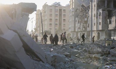 People walk in front of the husks of destroyed buildings