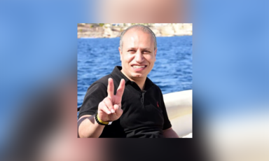 Smiling man gives V for victory sign with his hand while sitting in front of a body of water