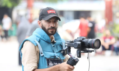 The photographer Mohammad Yaghi carrying a camera and wearing a vest marked Press 