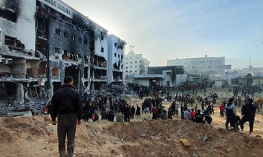 People stand in front of a burned-out hospital building