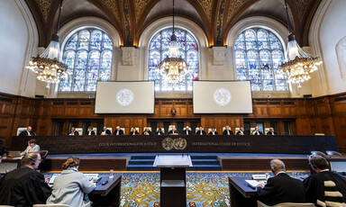 Judges sit at a long table below stained-glass windows in wood-paneled courtroom