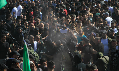 Man is carried on the shoulders of men in a big crowd of people carrying flags and weapons