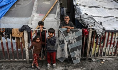 Three children and one adult stand beside a makeshift tent in southern Gaza 