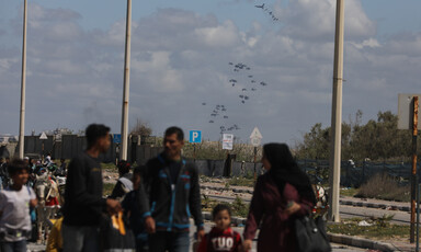 A group of people walk as parachuted packages are visible in the air behind them