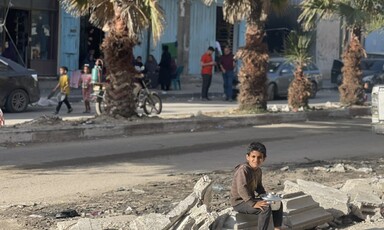 A boy sits on the side of a road, holding a pot. 