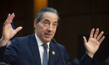 Congressman Jamie Raskin, holding a pen, raises his hands