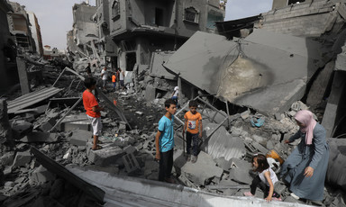 Women and children in brightly colored clothing stand on and walk over concrete rubble