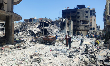 Two adults stand and one child sits down amid what remains of buildings that have been attacked in Gaza City 