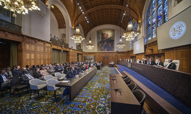 A wide angle view of an audience seated before a panel of judges in an ornately decorated courtroom