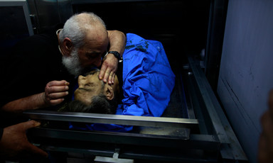A man leans over to kiss the face of a deceased male inside a hospital morgue refrigerator.
