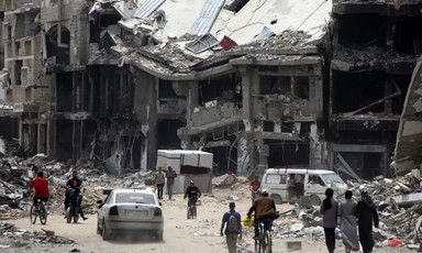 A collapsed building looms large as people walk down a street
