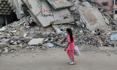 A girl walks past the remains of a building which has some graffiti written on it 
