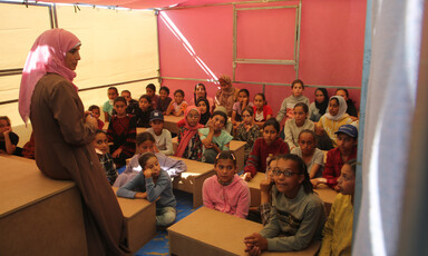 A teacher and children in a tent serving as a classroom 