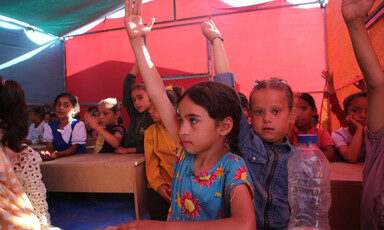 A few girls hold up their hands in a classroom inside a tent 