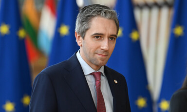 Ireland's Prime Minister Simon Harris stands before flags bearing the European Union's emblem