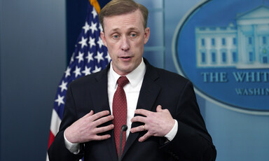 Jake Sullivan holds his hands towards his chest while standing in front of a US flag