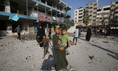 A woman holds a toddler while standing in front of damaged school