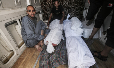 Two men sit beside corpses wrapped in shrouds 