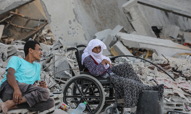 A woman in a wheelchair and a man sit in what remains of a building destroyed by Israel 