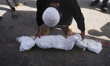 A man bends down to touch the shroud covering the body of a dead child