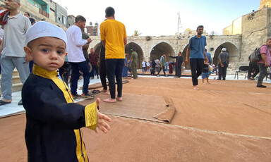 A boy stands with many adults behind him at the Grand Mosque of Gaza City 