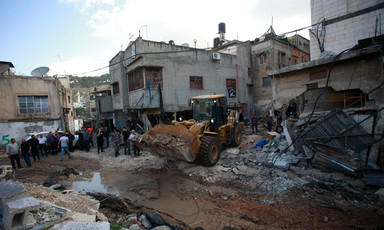 A bulldozer between buildings in a badly damaged Palestinian refugee camp