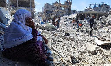 A woman is seated and is overlooking the rubble and debris around her