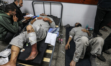 Men with bandaged arms and legs wearing grey prison clothes seen lying down