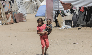 A child holds a smaller child beside a number of tents in Gaza 