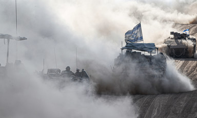 An Israeli tank in a cloud of smoke and dust flying an Israeli flag