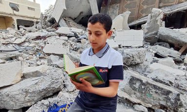 A boy reads a book amid the rubble of a house