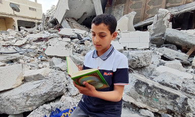 A boy reads a book amid the rubble of a house