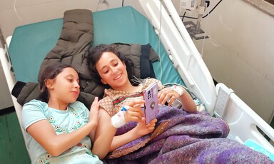 Two girls with a mobile phone lying on a hospital bed 