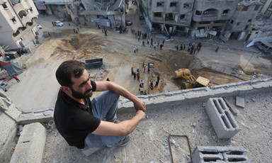 A man sits on a roof inspecting damage after airstrikes
