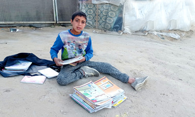 A boy sitting on the ground behind a pile of schoolbooks 