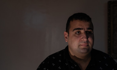 A man in a dimly lit room looks at the camera