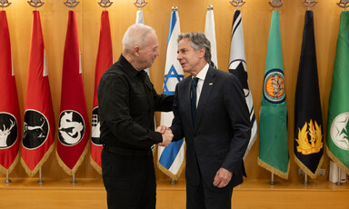 Gallant and Blinken shake hands while standing in front of Israeli military flags