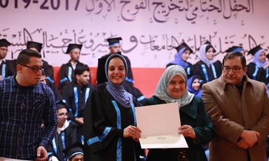 A young woman poses at a graduation ceremony holding her diploma