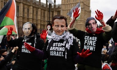 People wear masks showing the faces of politicians and T-shirts saying Stop Arming Israel and Ceasefire Now 