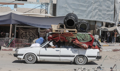 A white car weighed down with belongings strapped to its roof