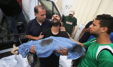A man cries while tipping his head back and holding the shrouded body of a child